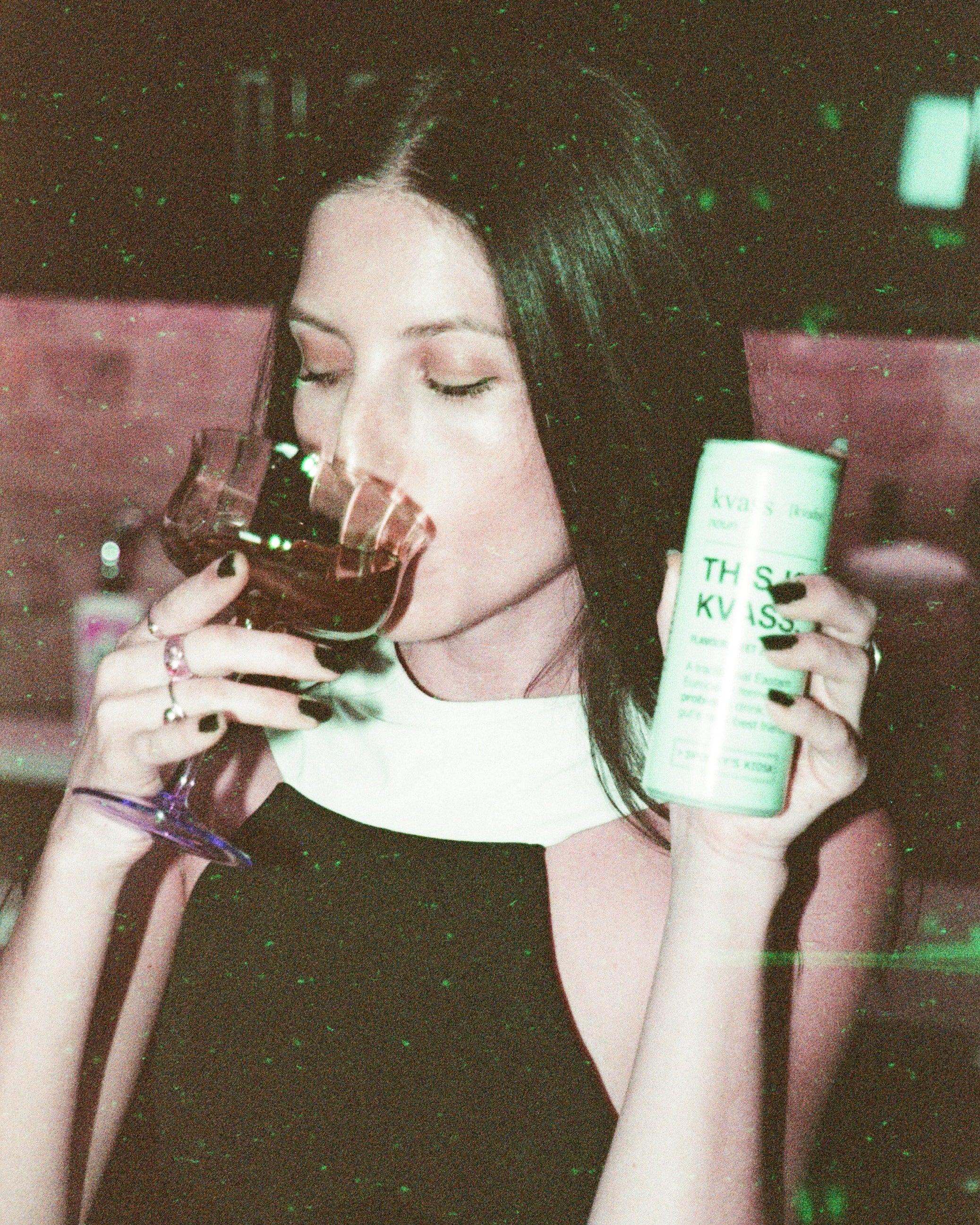 Woman holding a glass of red wine and a can of 'This Is KVASS' in a dark setting