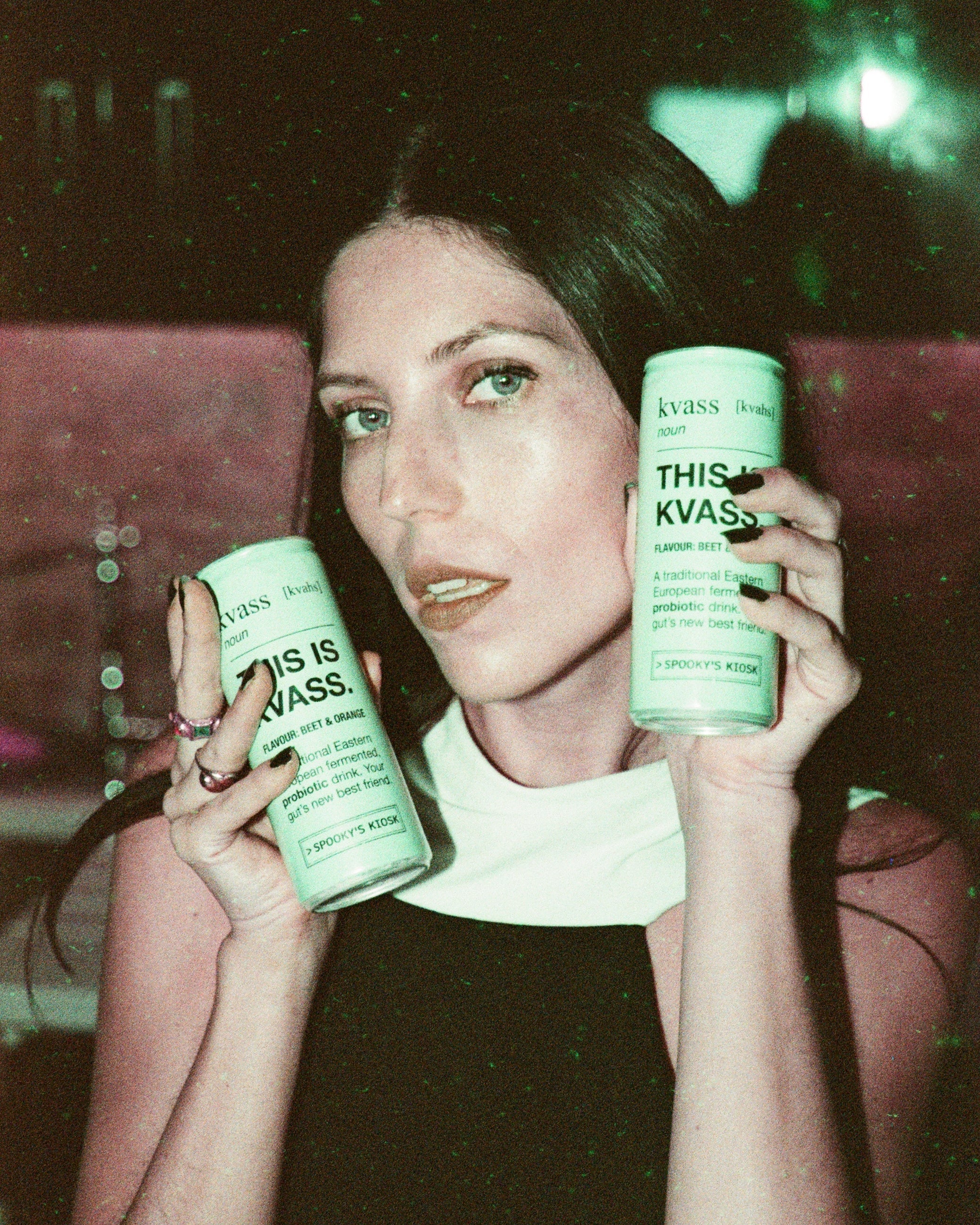 Woman holding two cans of Kvass in a dark setting