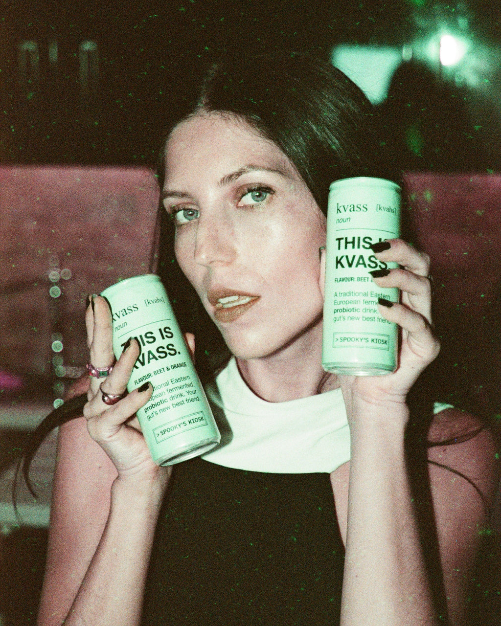 Woman holding two cans of Kvass in a dark setting