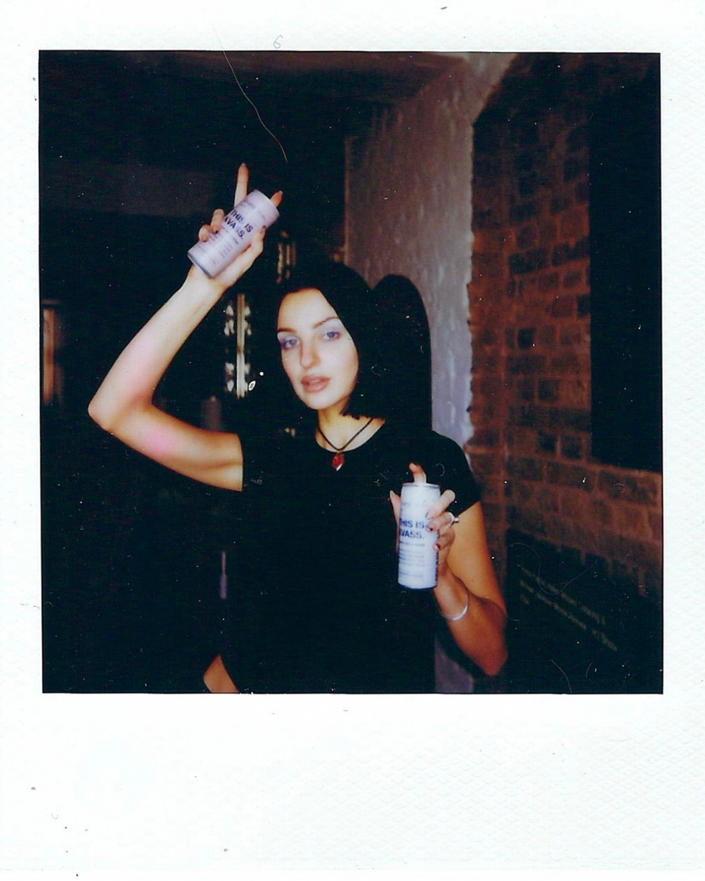 Polaroid-style photo of artist Vilte fuller holding two cans of this is kvass by Spooky’s kiosk against a dark backgroun