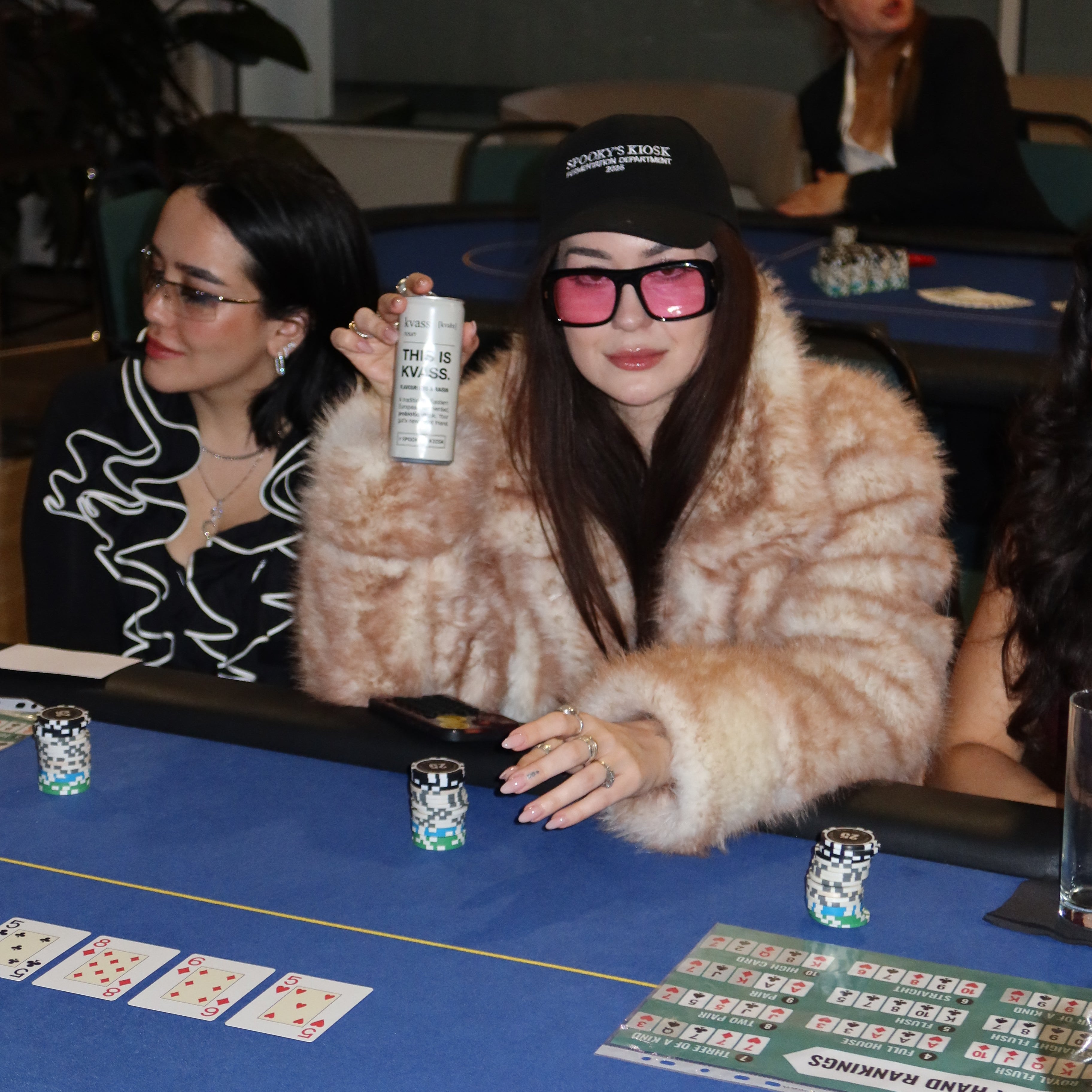 Two women at a casino table with drinks, surrounded by gaming elements.