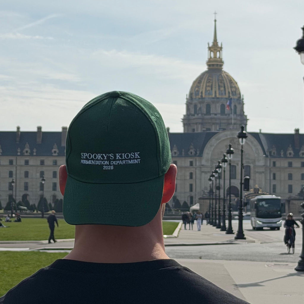 Person wearing a green cap with 'spooky's Kiosk' logo, facing a large building with a dome. Paris